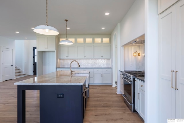 kitchen with pendant lighting, a center island with sink, high end stove, and white cabinets