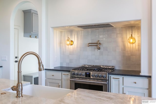 kitchen with high end stainless steel range, sink, dark stone countertops, and white cabinetry