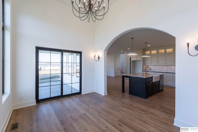 kitchen with an island with sink, a high ceiling, decorative light fixtures, dark hardwood / wood-style floors, and a chandelier