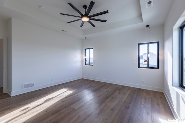 unfurnished room with a tray ceiling, dark wood-type flooring, ceiling fan, and plenty of natural light