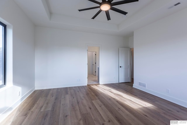 unfurnished room with ceiling fan, light wood-type flooring, and a raised ceiling