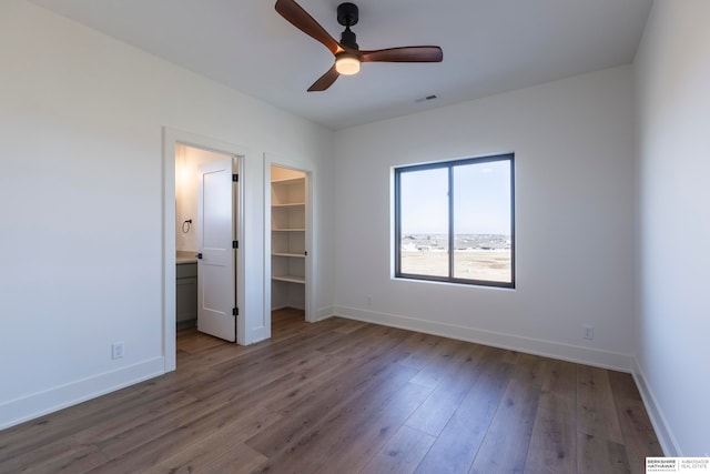 unfurnished bedroom featuring a closet, connected bathroom, a walk in closet, hardwood / wood-style floors, and ceiling fan