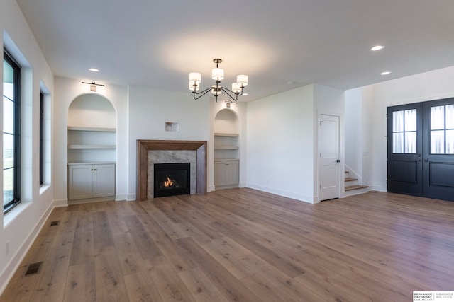 unfurnished living room featuring light hardwood / wood-style flooring, a high end fireplace, a chandelier, and built in features