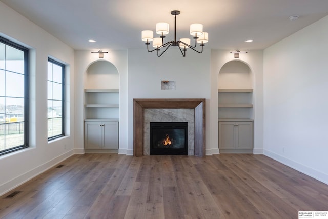 unfurnished living room featuring built in shelves, a chandelier, light hardwood / wood-style floors, and a fireplace