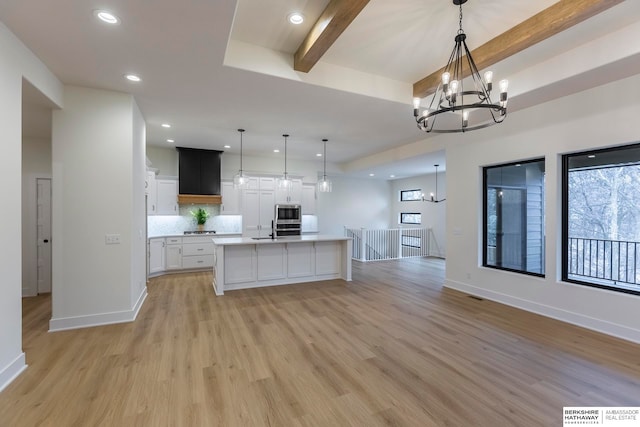 kitchen featuring white cabinets, beamed ceiling, an island with sink, hanging light fixtures, and light hardwood / wood-style flooring