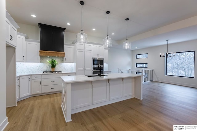 kitchen with light hardwood / wood-style floors, a kitchen island with sink, sink, white cabinetry, and hanging light fixtures