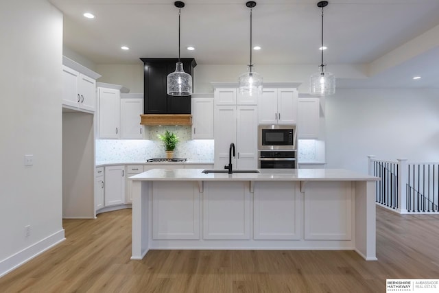 kitchen with appliances with stainless steel finishes, light hardwood / wood-style floors, an island with sink, and white cabinets