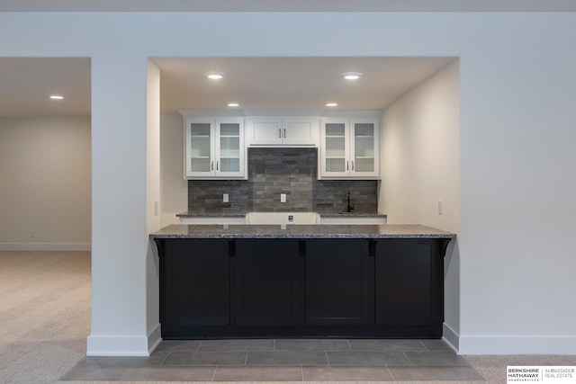 kitchen featuring kitchen peninsula, stone countertops, white cabinetry, light carpet, and decorative backsplash