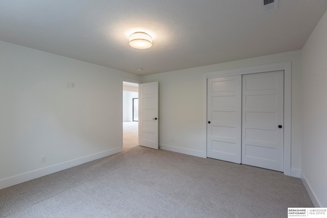 unfurnished bedroom with light carpet, a textured ceiling, and a closet