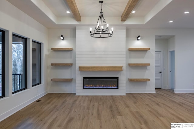 unfurnished living room featuring light wood-type flooring, a large fireplace, beamed ceiling, and a notable chandelier