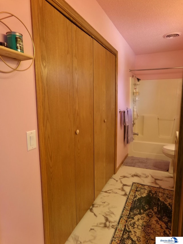 bathroom with a textured ceiling,  shower combination, and toilet