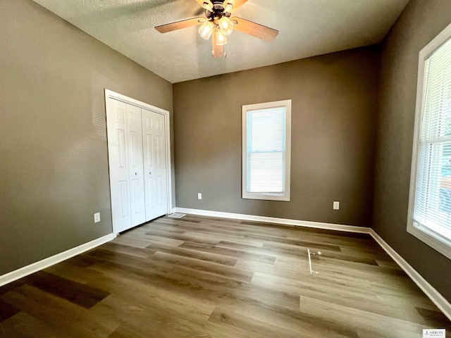 unfurnished bedroom with multiple windows, wood-type flooring, and ceiling fan