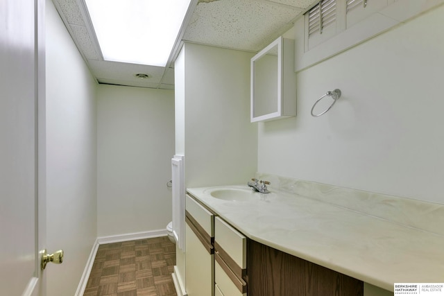 bathroom featuring a drop ceiling, parquet floors, vanity, and toilet