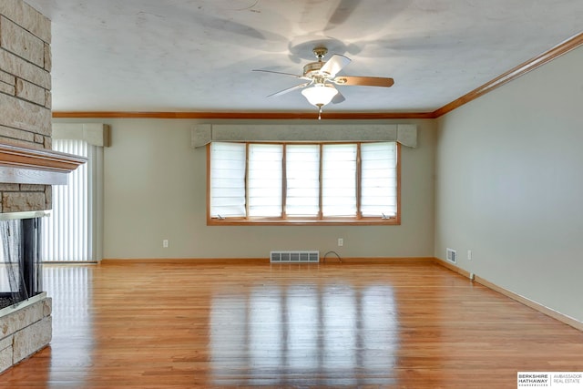 unfurnished living room featuring crown molding, ceiling fan, a stone fireplace, and light hardwood / wood-style floors