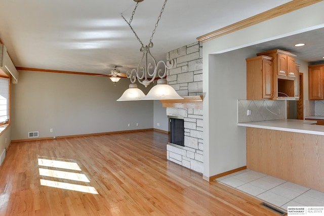 kitchen featuring a stone fireplace, ornamental molding, and light hardwood / wood-style floors