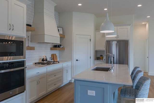 kitchen with white cabinetry, an island with sink, stainless steel appliances, decorative light fixtures, and sink