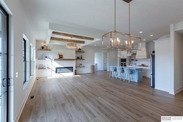 unfurnished living room with light hardwood / wood-style floors, beam ceiling, a fireplace, and a chandelier