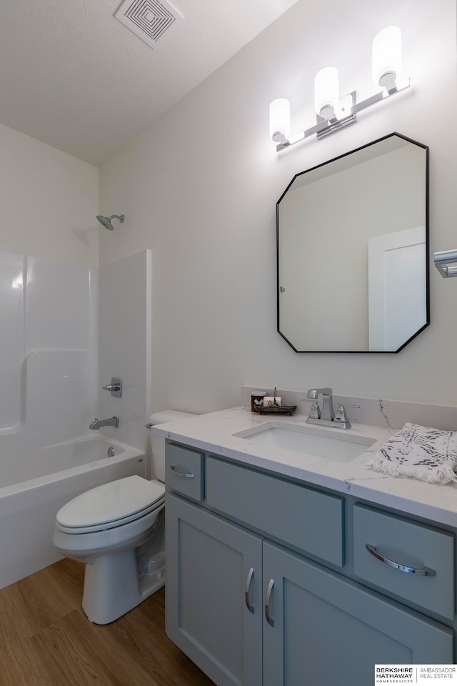 full bathroom featuring a textured ceiling, bathing tub / shower combination, hardwood / wood-style floors, vanity, and toilet