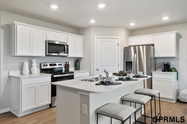 kitchen featuring white cabinets, stainless steel appliances, light hardwood / wood-style flooring, a kitchen island with sink, and sink