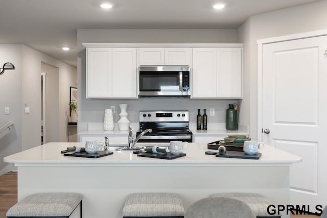 kitchen with white cabinets, a center island with sink, appliances with stainless steel finishes, a kitchen bar, and dark hardwood / wood-style flooring