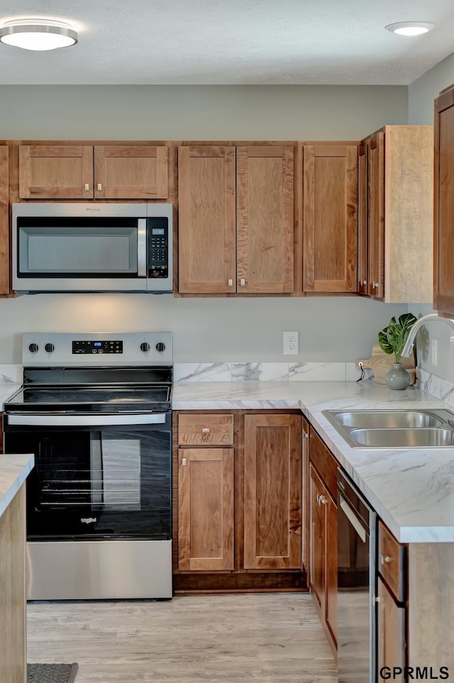 kitchen featuring appliances with stainless steel finishes, a textured ceiling, light hardwood / wood-style flooring, and sink