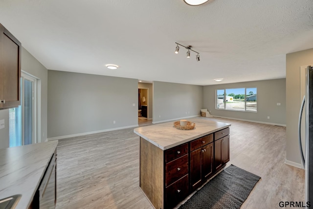 kitchen featuring a textured ceiling, dark brown cabinetry, light hardwood / wood-style flooring, butcher block countertops, and a kitchen island