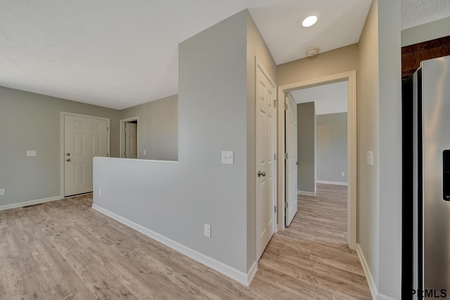 corridor with a textured ceiling and light hardwood / wood-style flooring