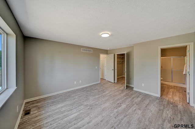 unfurnished bedroom featuring light wood-type flooring, a spacious closet, a textured ceiling, and a closet