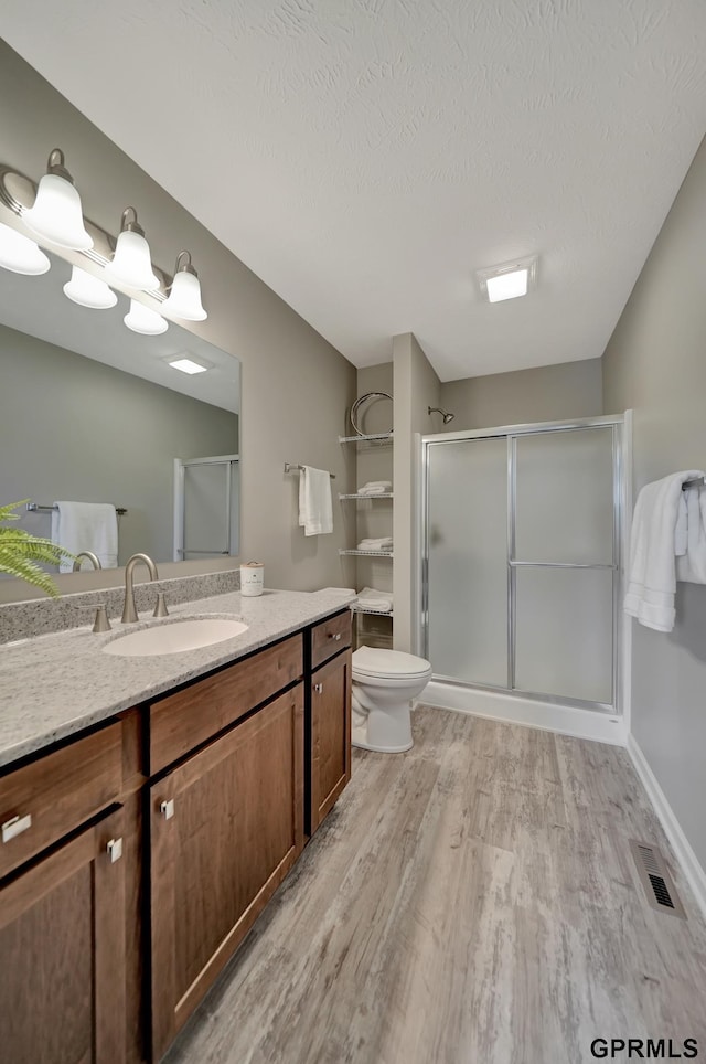 bathroom with vanity, a textured ceiling, wood-type flooring, toilet, and a shower with shower door