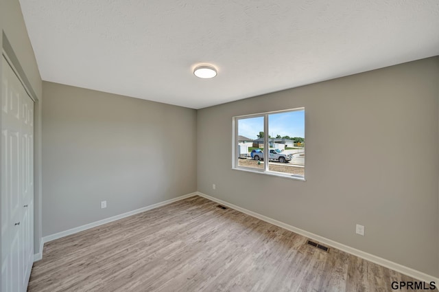 unfurnished bedroom with a textured ceiling, light hardwood / wood-style flooring, and a closet