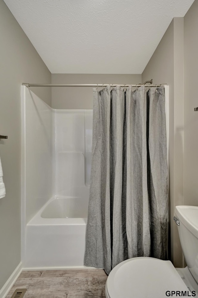 bathroom with hardwood / wood-style flooring, toilet, and shower / bathtub combination with curtain