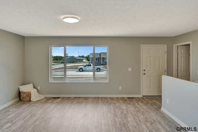 empty room with a textured ceiling and light hardwood / wood-style flooring