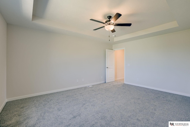 carpeted spare room featuring a raised ceiling and ceiling fan