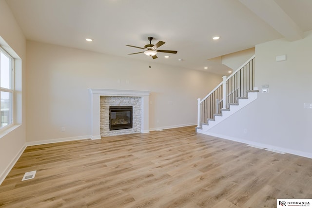 unfurnished living room with ceiling fan, a stone fireplace, light hardwood / wood-style floors, and beam ceiling