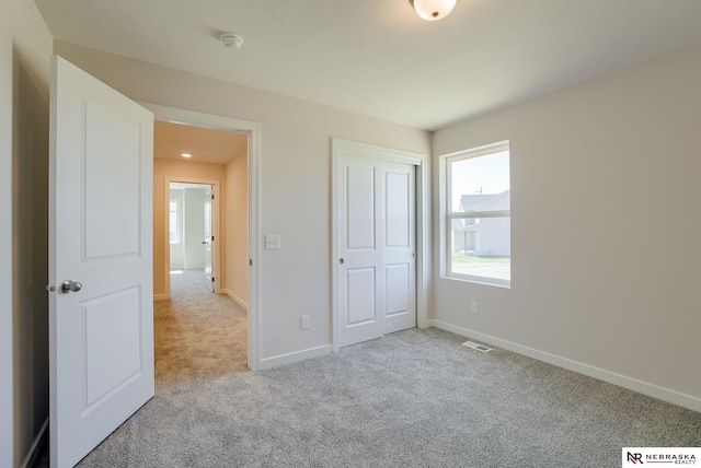 unfurnished bedroom with light colored carpet and a closet