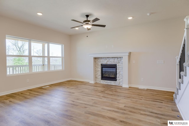 unfurnished living room featuring ceiling fan, a stone fireplace, and light hardwood / wood-style flooring