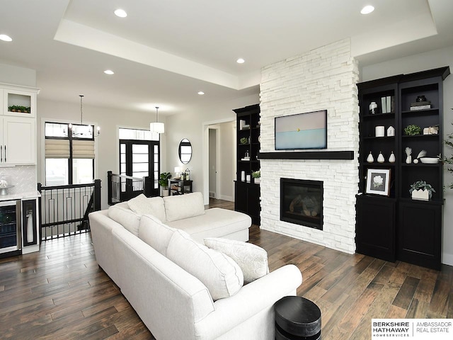 living room with a raised ceiling, dark hardwood / wood-style floors, and a stone fireplace