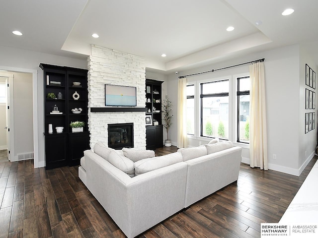 living room with a fireplace, a tray ceiling, and dark hardwood / wood-style flooring