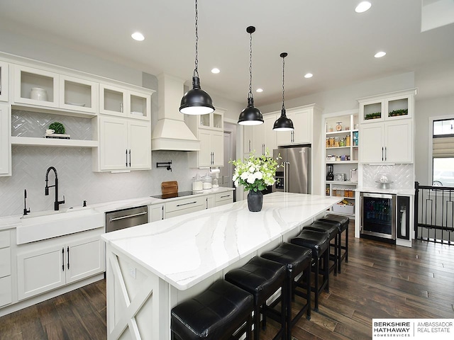 kitchen featuring premium range hood, sink, white cabinetry, appliances with stainless steel finishes, and a center island