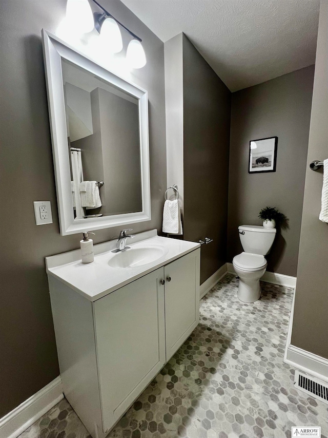 bathroom with a textured ceiling, vanity, and toilet