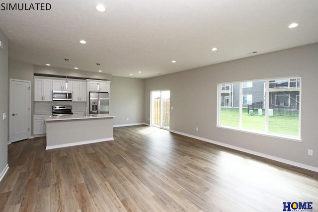 kitchen with light wood-type flooring, stainless steel appliances, white cabinetry, and a kitchen island