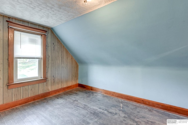 additional living space featuring a textured ceiling, wood-type flooring, wood walls, and vaulted ceiling