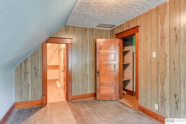 bonus room with wood-type flooring, lofted ceiling, a textured ceiling, and wood walls