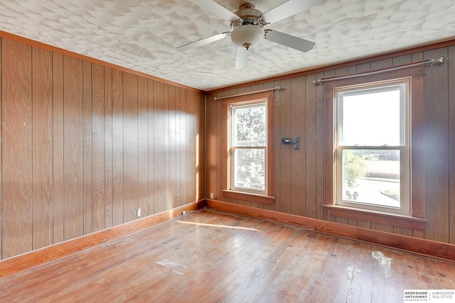 unfurnished room with ceiling fan, wooden walls, and wood-type flooring