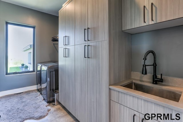 clothes washing area featuring cabinets, light hardwood / wood-style floors, washer and clothes dryer, and sink