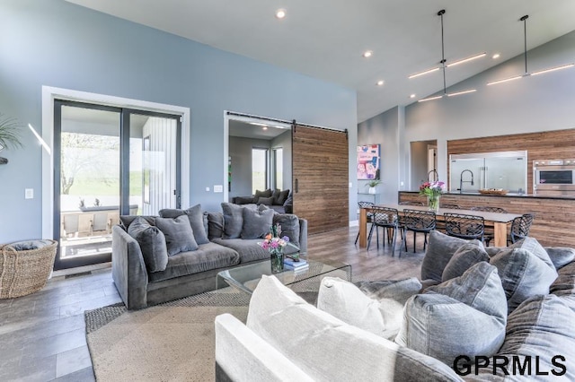 living room featuring high vaulted ceiling, sink, hardwood / wood-style flooring, and a barn door