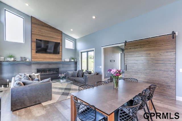 dining area featuring a barn door, light wood-type flooring, wood walls, and high vaulted ceiling