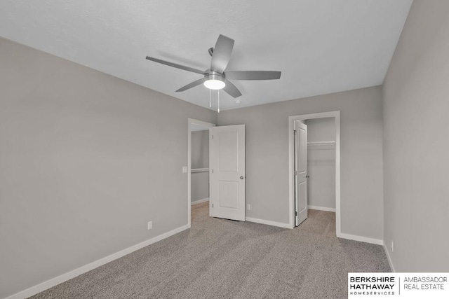 unfurnished bedroom with a closet, ceiling fan, a spacious closet, and light carpet