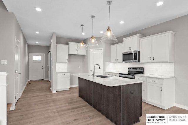 kitchen with sink, white cabinets, hanging light fixtures, a kitchen island with sink, and appliances with stainless steel finishes