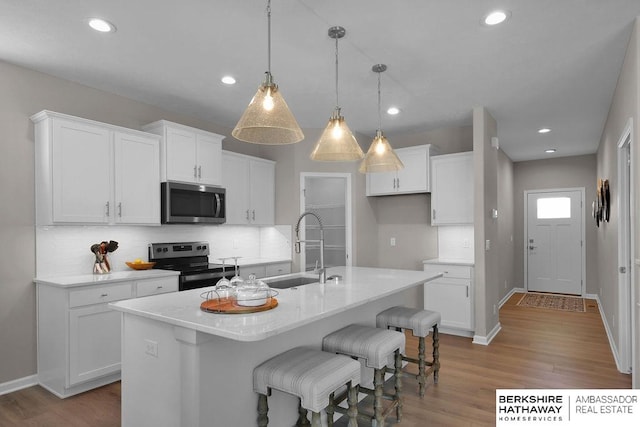 kitchen with white cabinets, stainless steel appliances, a kitchen island with sink, and pendant lighting